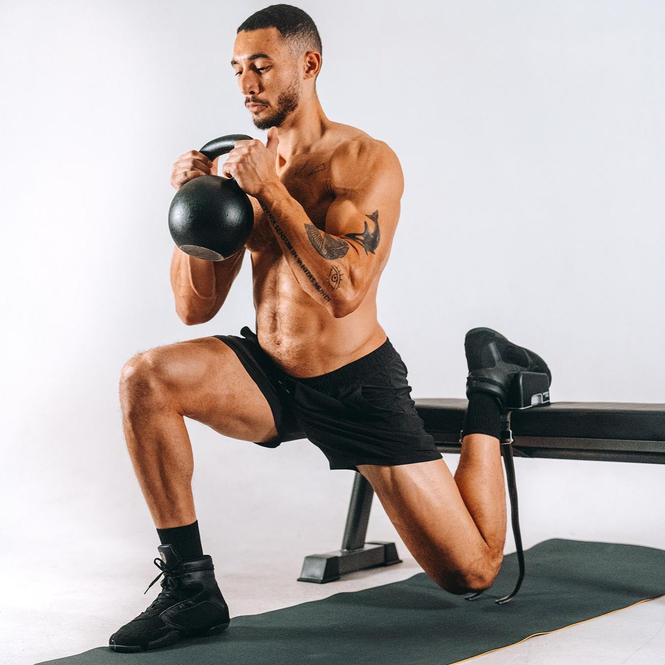 Man exercising with a kettlebell with foot placed on the ARC with a white background