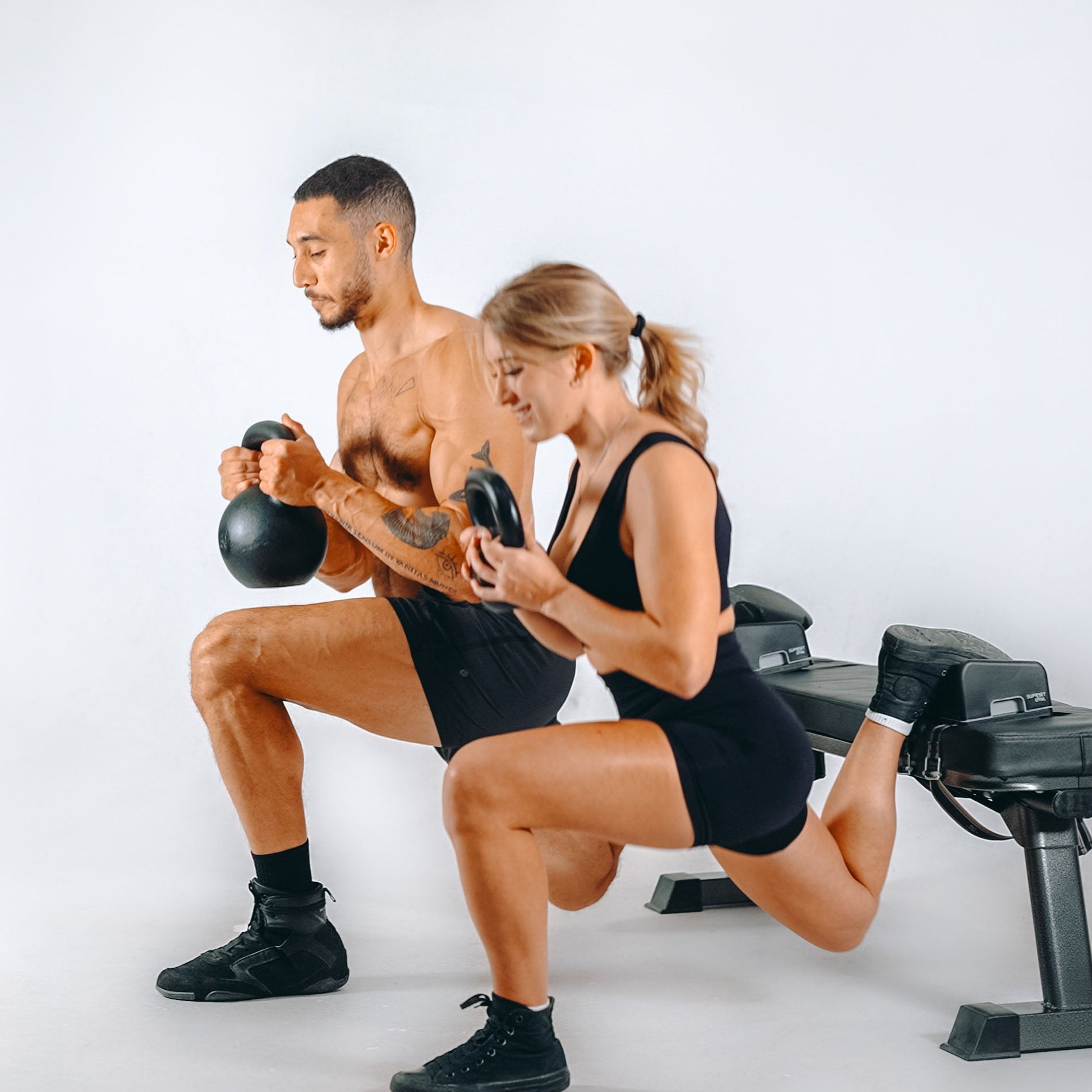 Two people exercising with kettlebells, foot placed on ARC with a white background