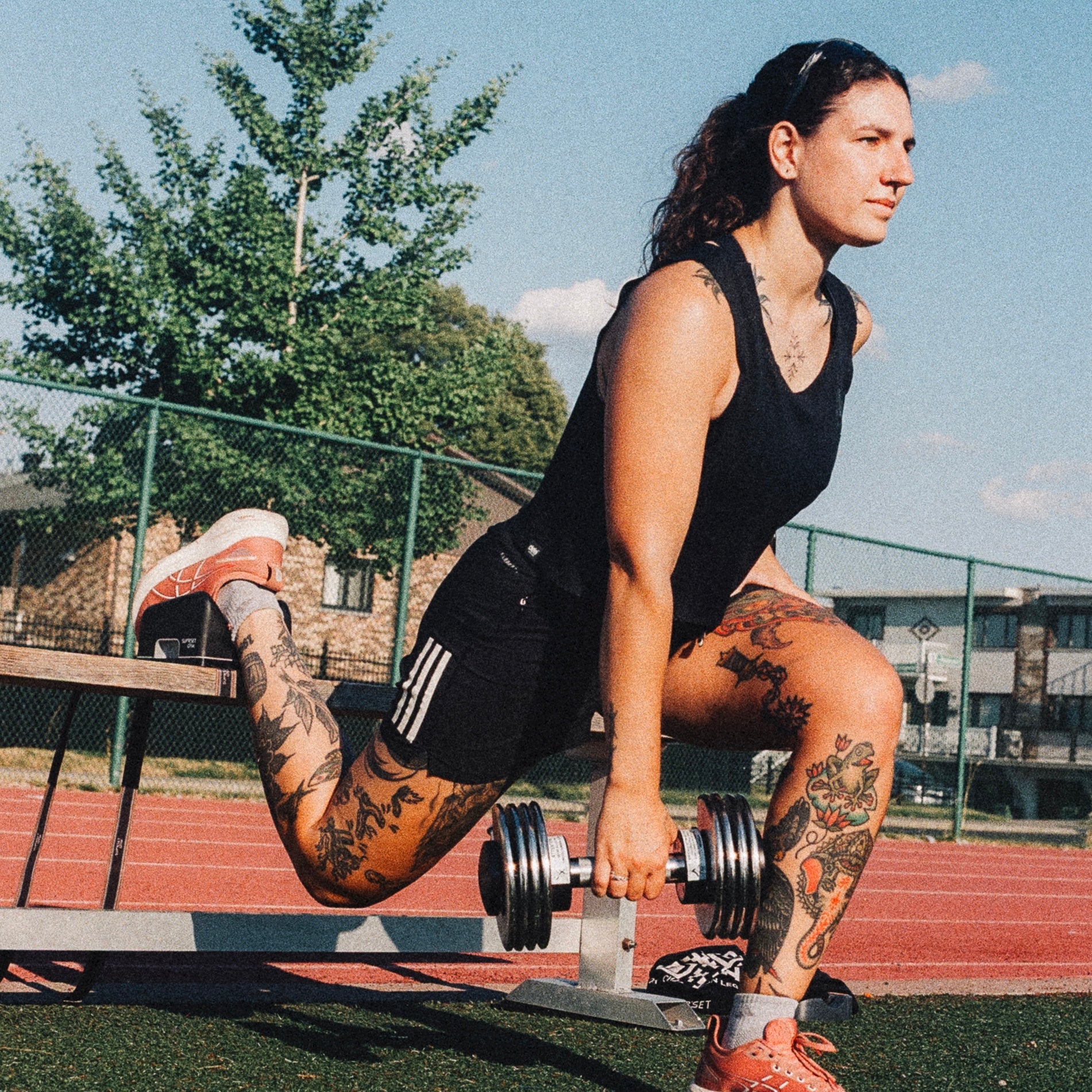 Woman in athletic wear doing the Bulgarian split squat with Stability Block ARC exercising with a dumbbell outdoors on a sunny day